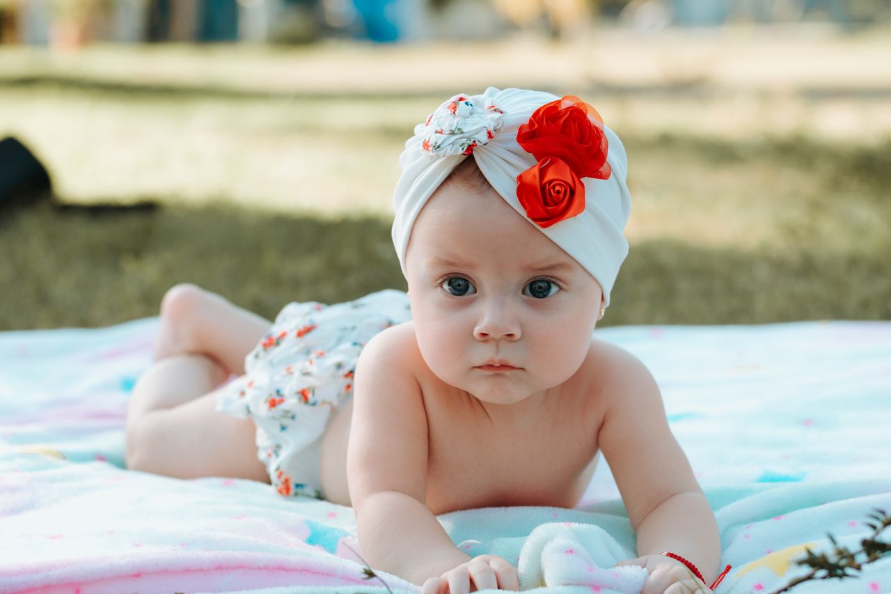 gallery-1 Cute baby in a floral turban lying on a blanket outdoors.
