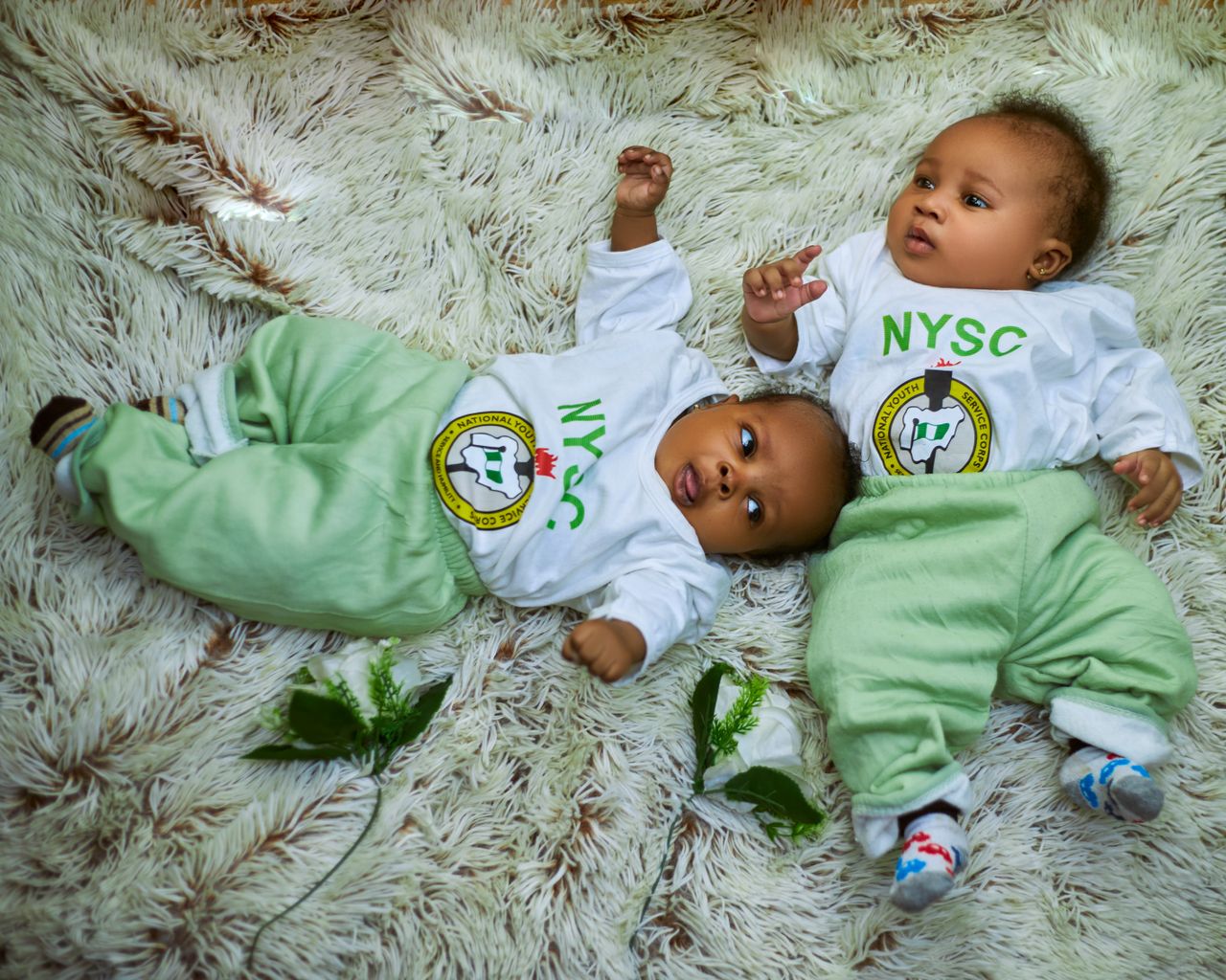 services-03 Adorable babies in NYSC attire lying on a cozy rug, representing innocence and national pride.
