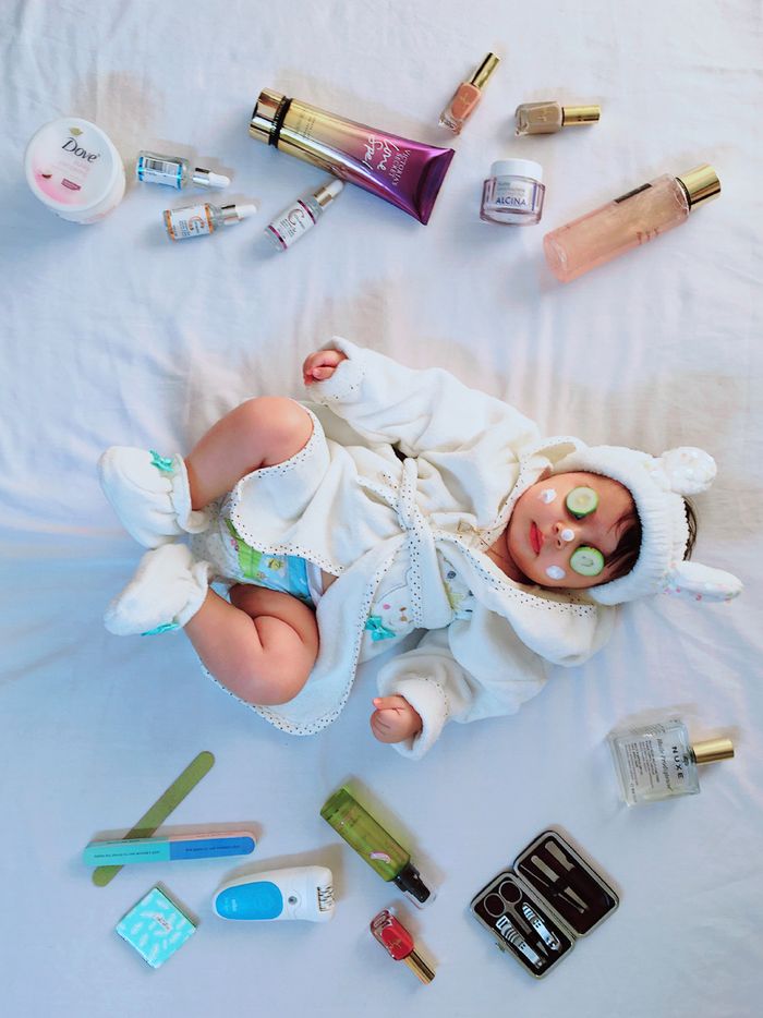 services-03 Cute baby with cucumber eye mask surrounded by skincare items on a bed.