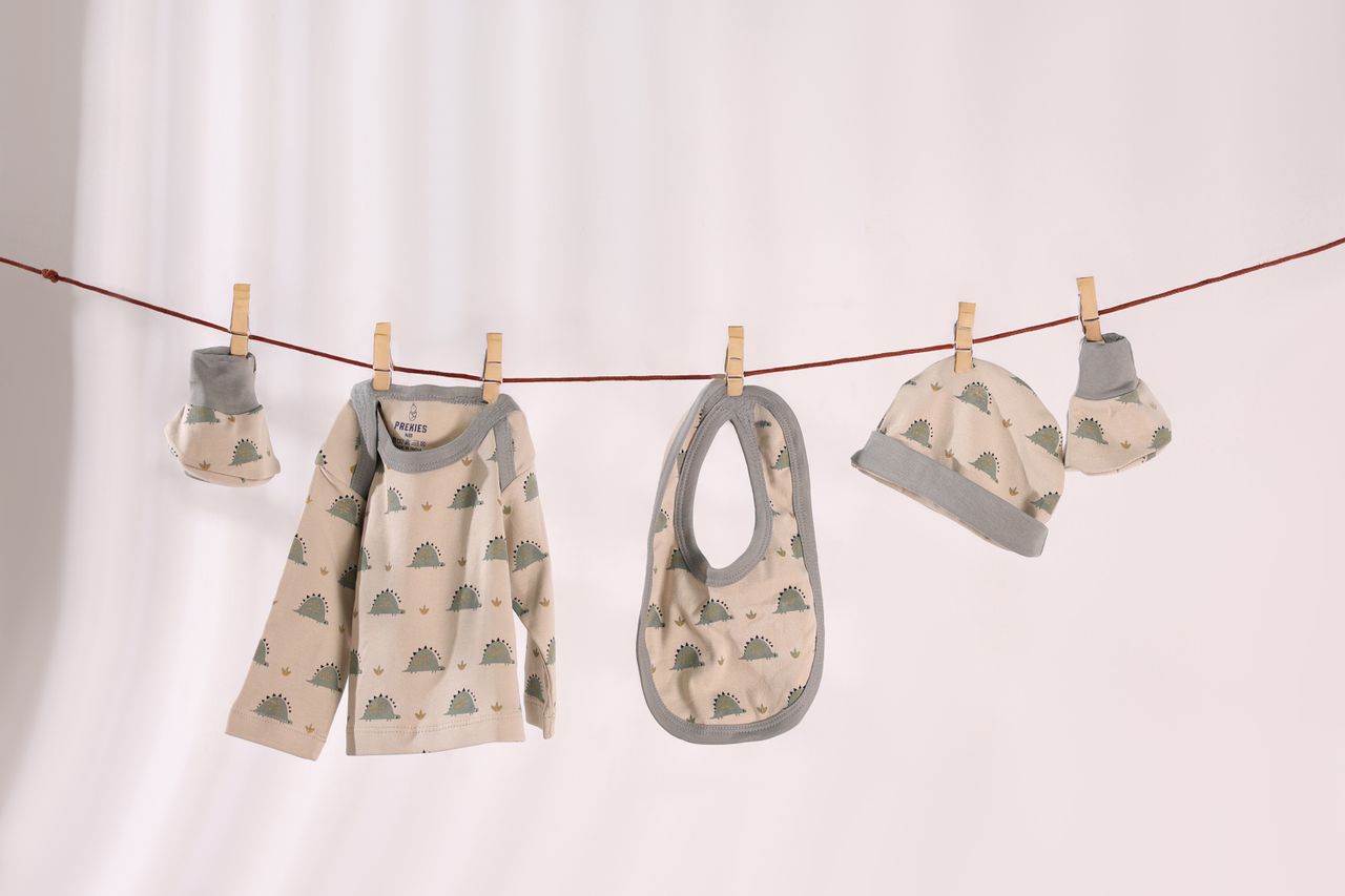hero-img-01 Baby clothes set with cute patterns hanging on a line against a white background.