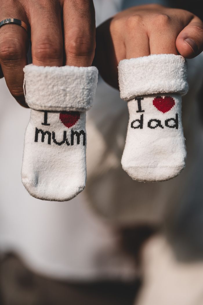 services-02 Adorable baby socks with 'I love mum' and 'I love dad' designs held by adults' hands.