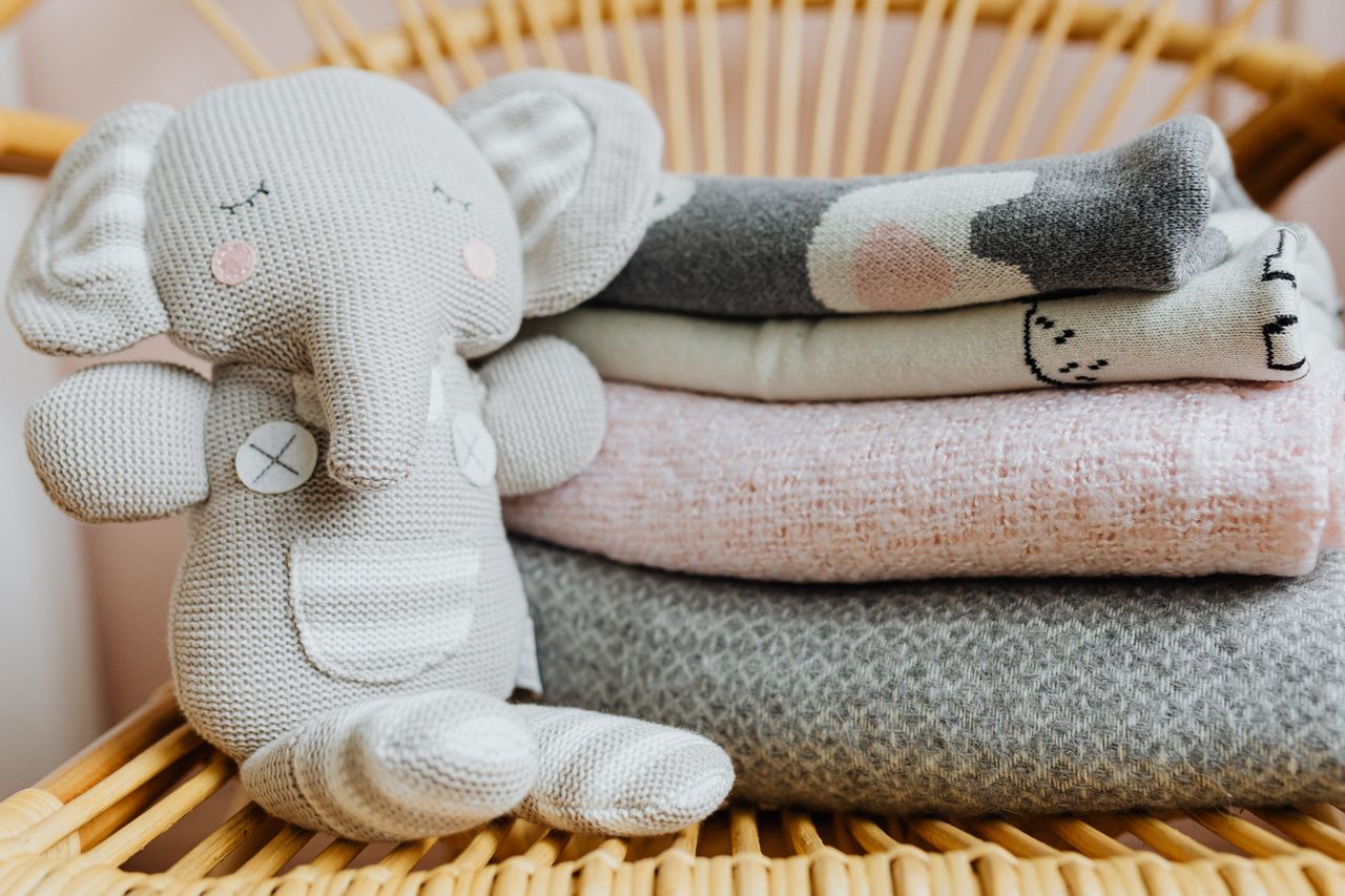 services-01 Cute knitted elephant toy and pastel blankets on a wicker chair, perfect for a cozy nursery.